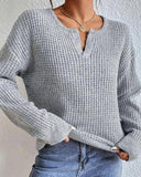 Person wearing a gray knitted sweater and blue jeans against a light background