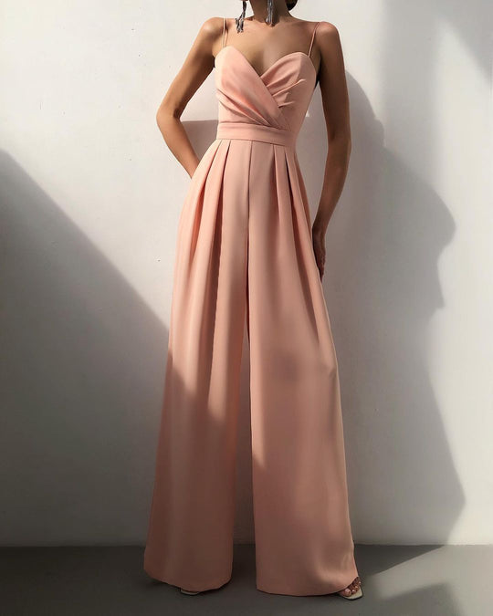 Woman wearing a long pink jumpsuit against a white wall