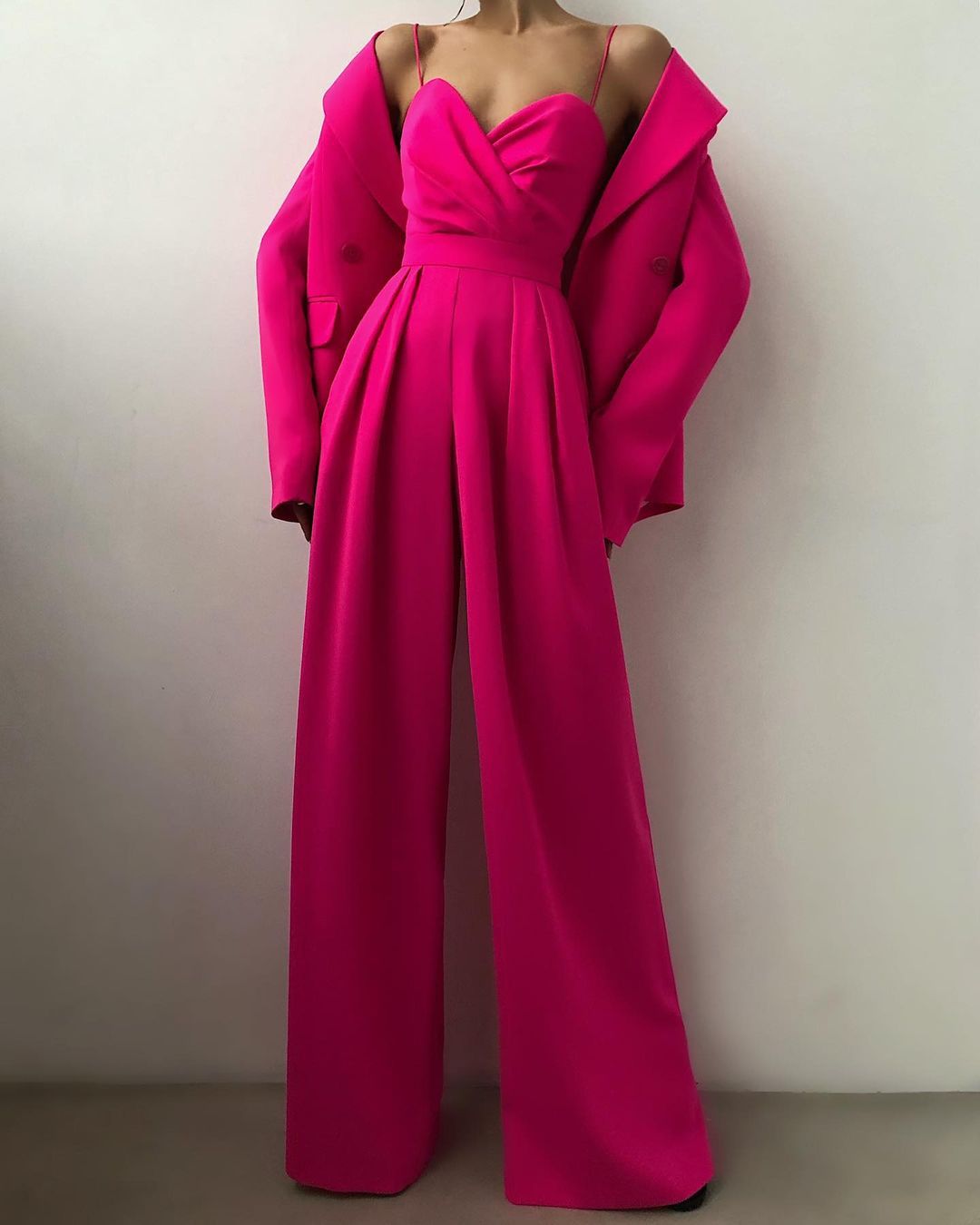 Person wearing a bright pink jumpsuit with a matching coat against a plain background