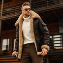 Man wearing a brown shearling jacket and sunglasses in front of a wooden building.