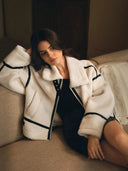 Woman wearing a white sherpa jacket with black accents sitting on a couch.