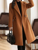 Person wearing a brown coat holding a black handbag indoors.