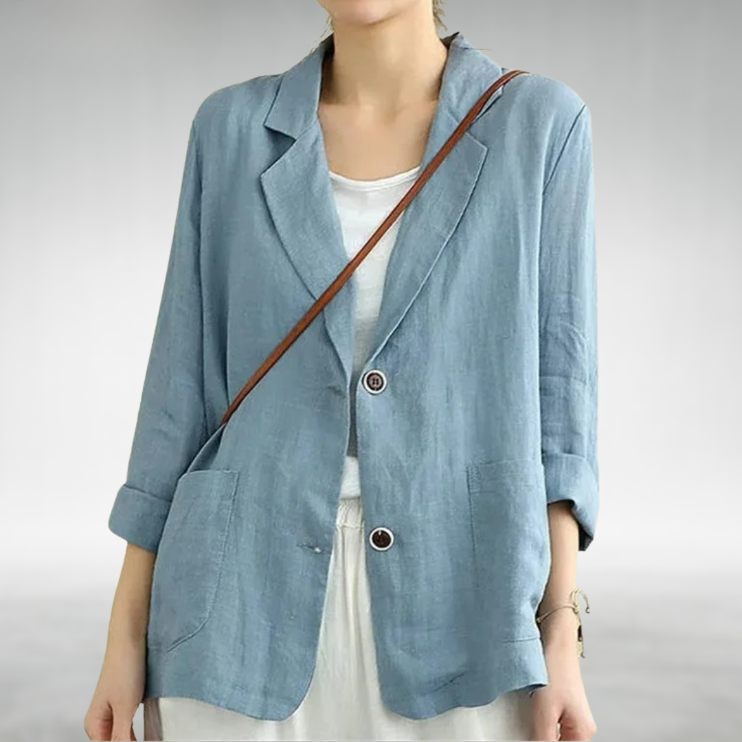 Person wearing a light blue blazer over a white shirt with a brown strap over the shoulder on a plain background.