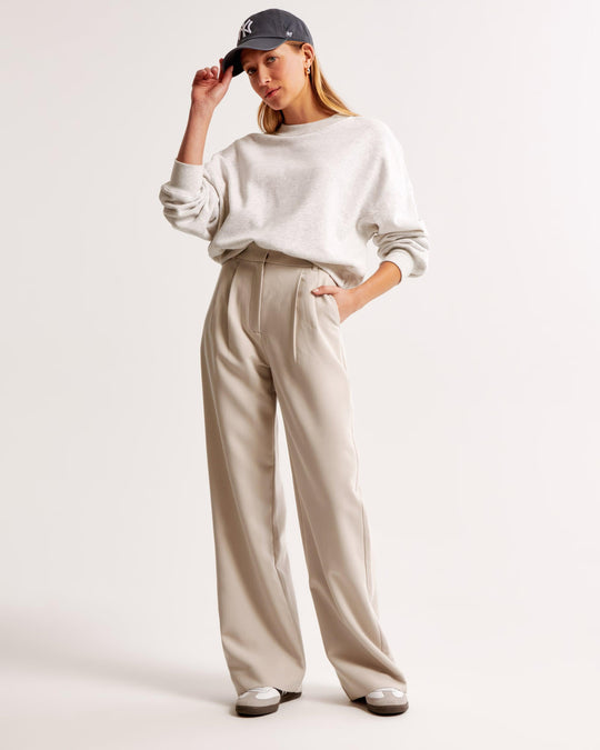 Woman wearing a white sweatshirt and beige pants with a cap on a light background