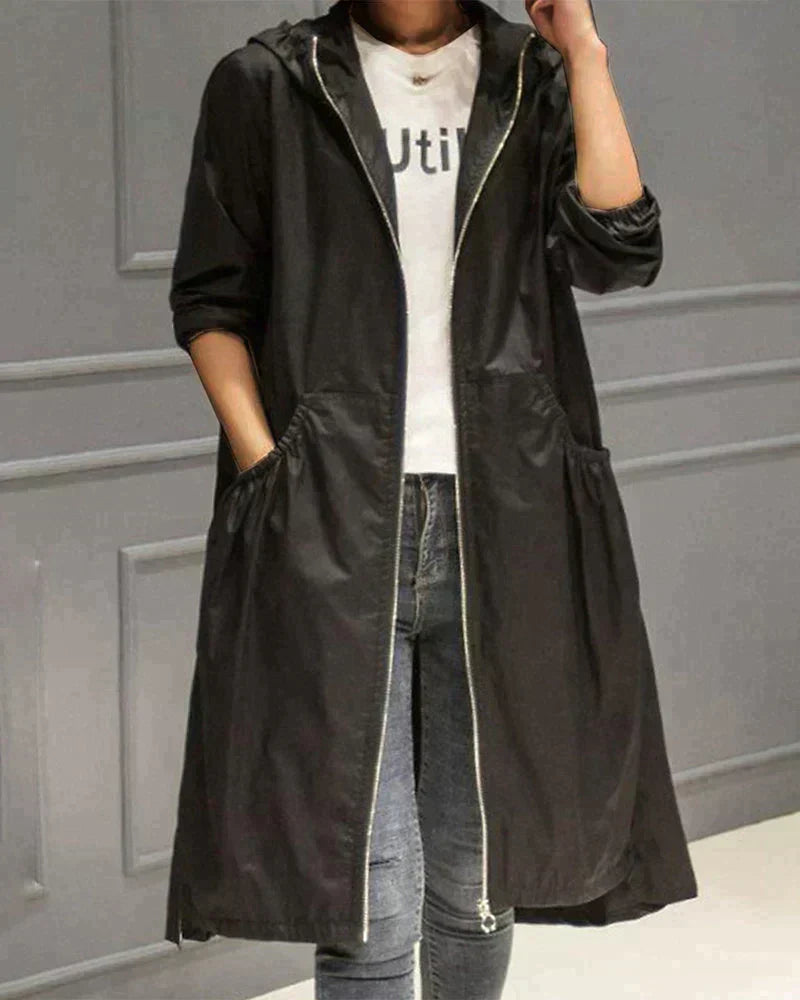 Person wearing a black hooded coat over a white shirt with text, standing against a gray wall.
