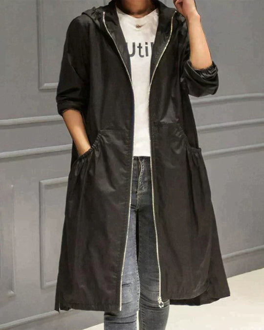 Person wearing a black hooded coat over a white shirt with text, standing against a gray wall.