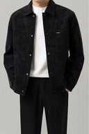 Person wearing a black suede jacket over a white shirt and black pants on a gray background