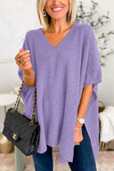 Woman wearing a purple oversized sweater holding a black handbag indoors.