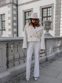 Woman in a white outfit with a hat standing in front of a stone building.