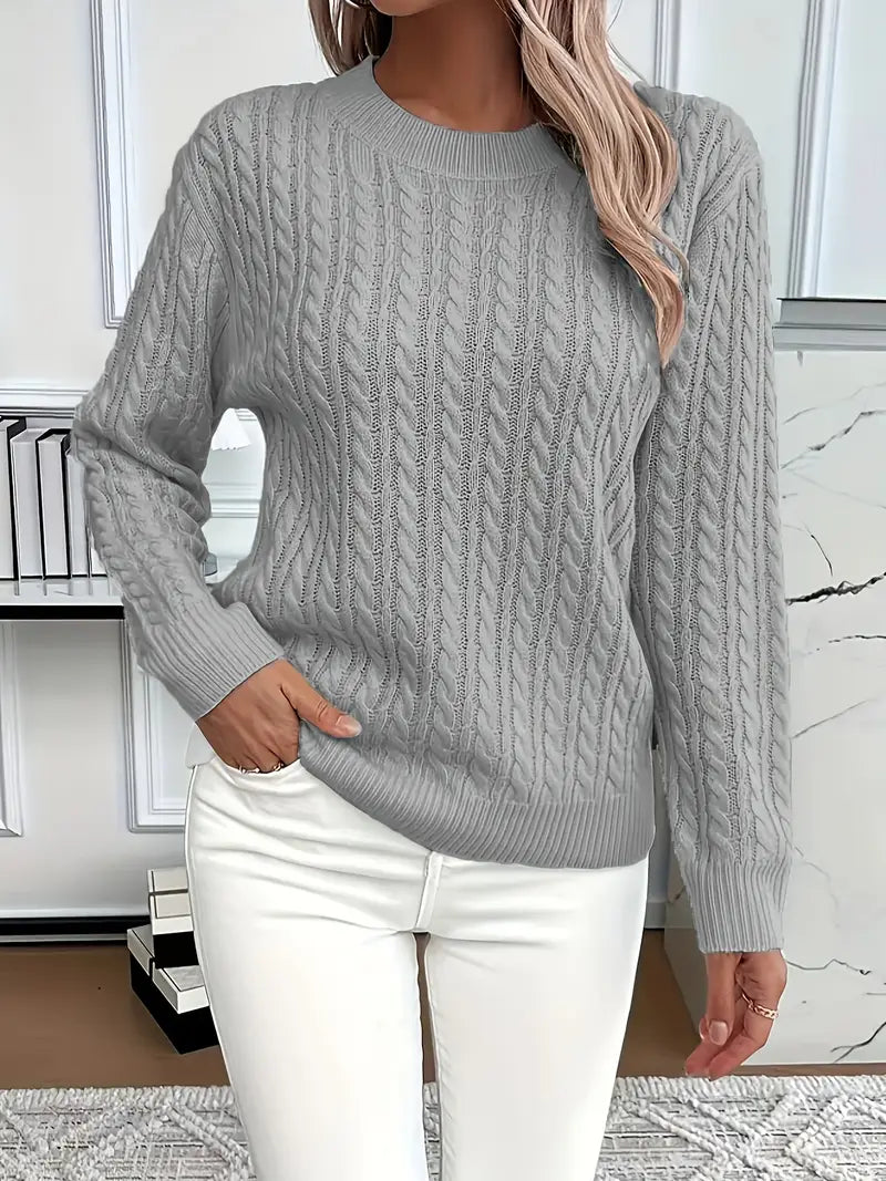Person wearing a gray cable knit sweater and white pants in an indoor setting.