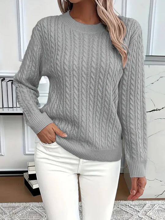 Person wearing a gray cable knit sweater and white pants in an indoor setting.