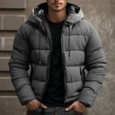 Man wearing a gray puffer jacket with a hood against a neutral background