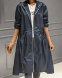 Person wearing a long navy raincoat against a gray wall.