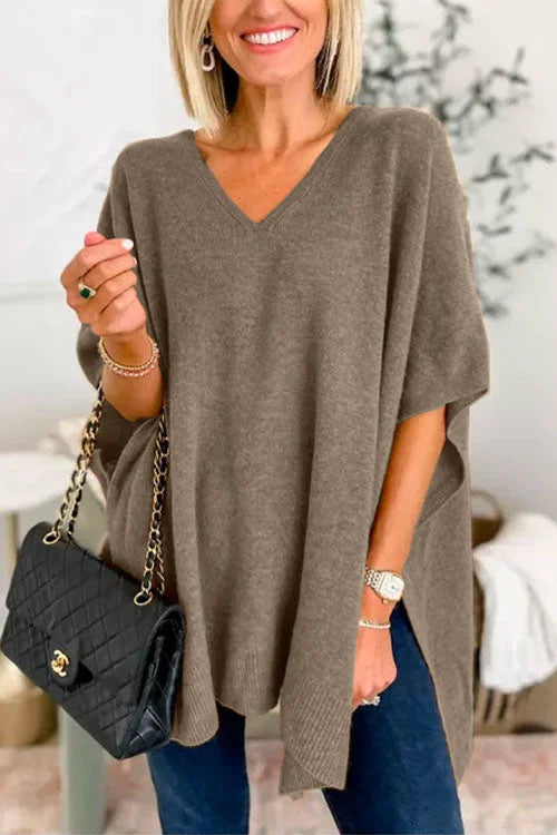 Woman wearing a brown poncho over a blue outfit, holding a black handbag.