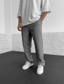 Person wearing a white oversized shirt and gray ribbed pants against a white wall.