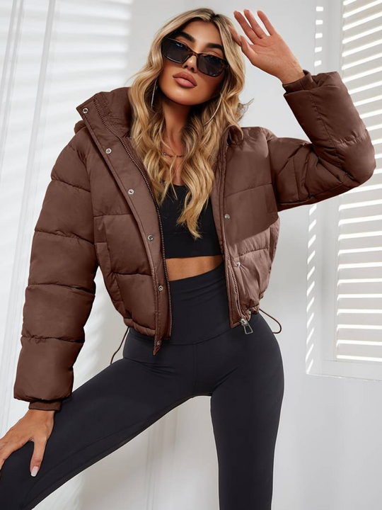 Woman wearing a brown puffer jacket and black leggings posing against a white background