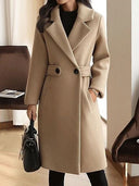 Person wearing a beige coat holding a black handbag indoors.