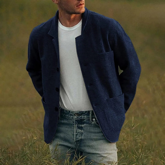 Man wearing a navy jacket over a white shirt and jeans in a grassy field