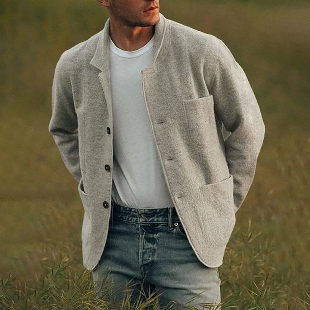Man wearing a beige cardigan over a white shirt and jeans in a grassy field