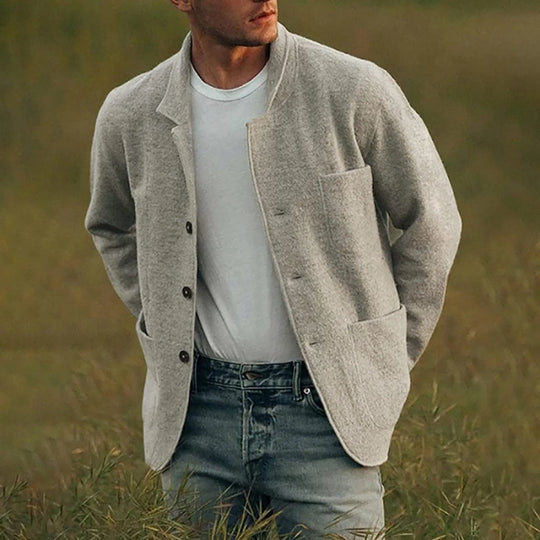 Man wearing a beige cardigan over a white shirt and jeans in a grassy field