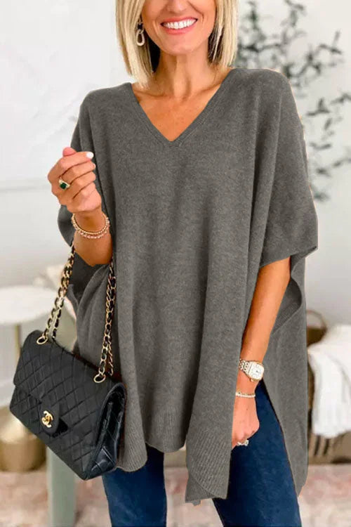 Woman wearing a gray poncho holding a black handbag indoors.