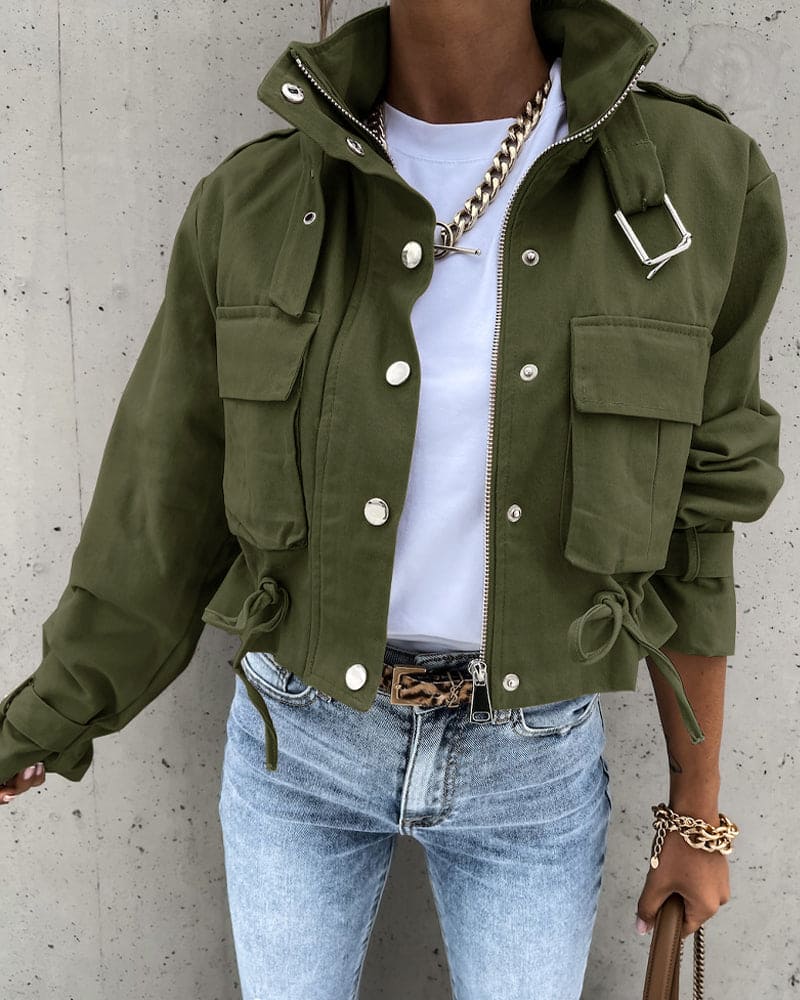 Person wearing a green jacket, white shirt, and blue jeans against a concrete wall.