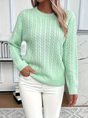 Person wearing a light green cable knit sweater and white pants in an indoor setting.