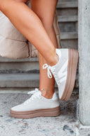 White sneakers with brown soles worn by a person sitting on steps.