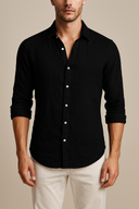 Man wearing a black button-up shirt with rolled-up sleeves and white pants on a beige background