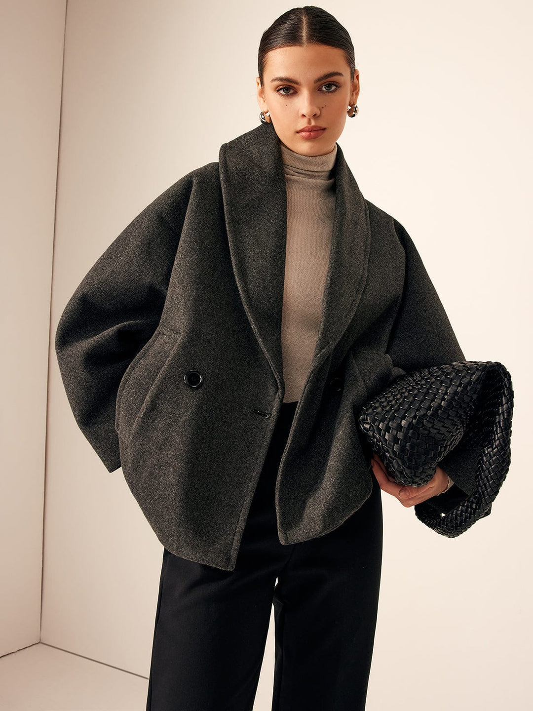 Woman wearing a gray coat holding a black clutch against a neutral background
