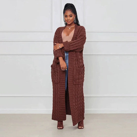 Woman wearing a long brown cardigan over a sheer top and jeans against a white background