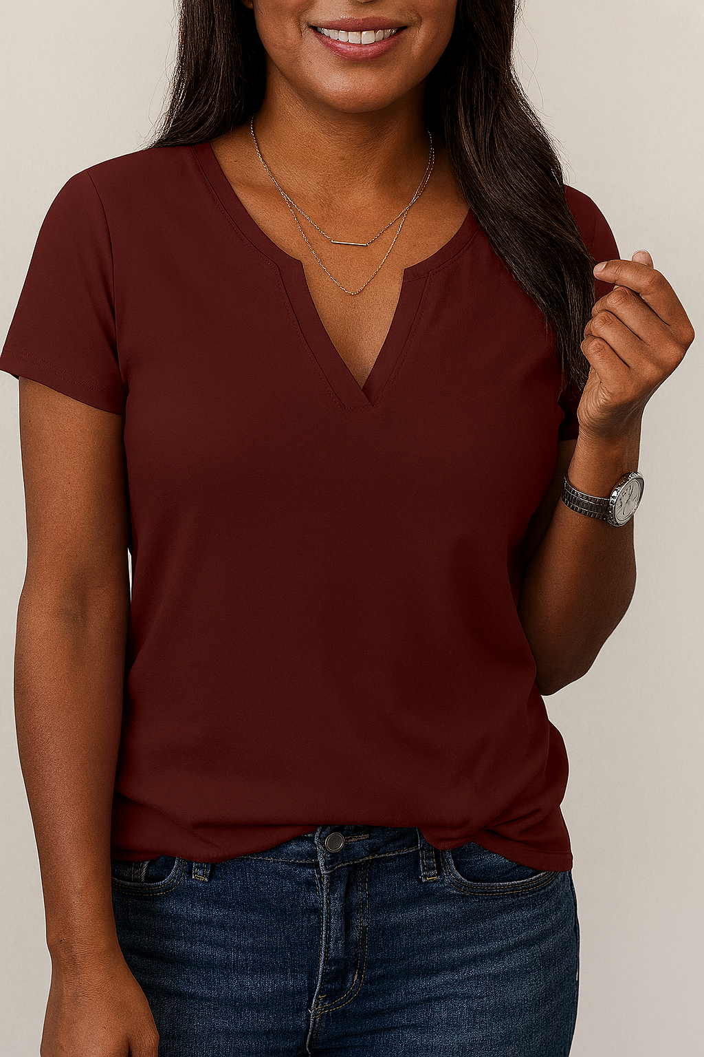 Woman wearing a maroon V-neck t-shirt and blue jeans against a neutral background