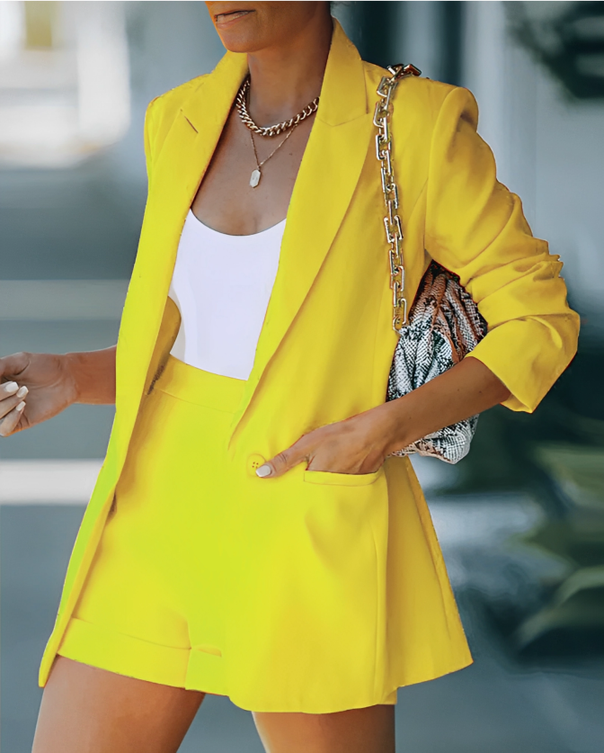 Person wearing a bright yellow outfit with a white top and skirt, holding a patterned clutch.
