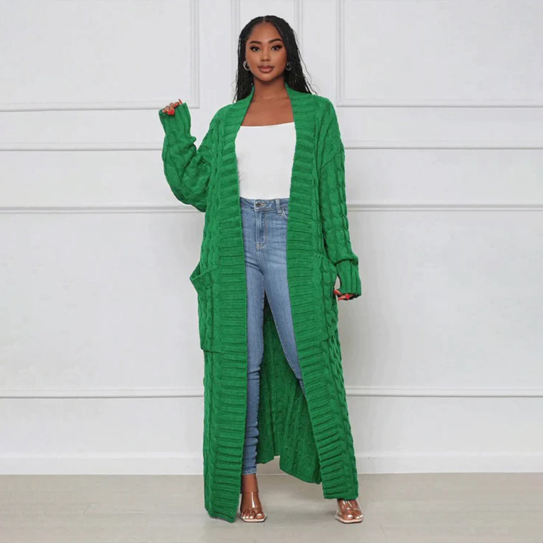 Woman wearing a long green cardigan over a white top and blue jeans against a white background