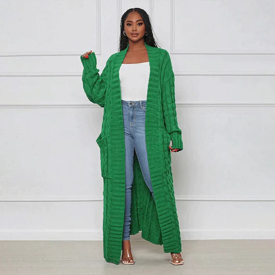 Woman wearing a long green cardigan over a white top and blue jeans against a white background