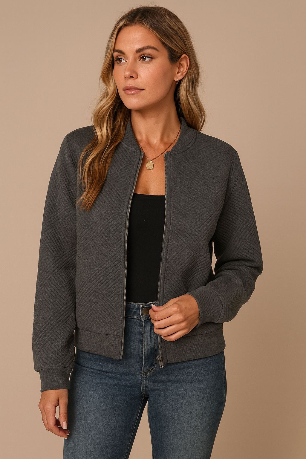 Woman wearing a dark gray jacket over a black top and blue jeans on a beige background