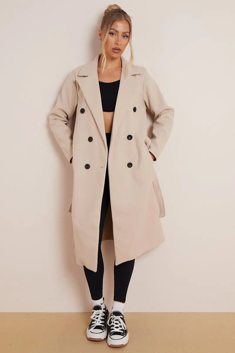 Woman wearing a long beige coat with black buttons on a plain background