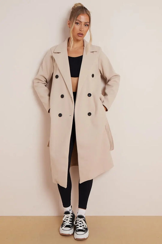 Woman wearing a long beige coat with black buttons on a plain background