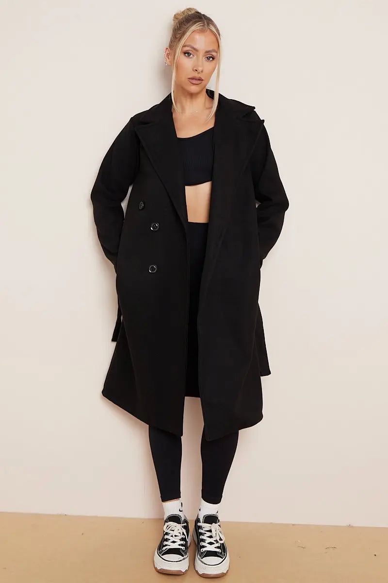 Person wearing a black coat, black top, and black pants against a white wall.