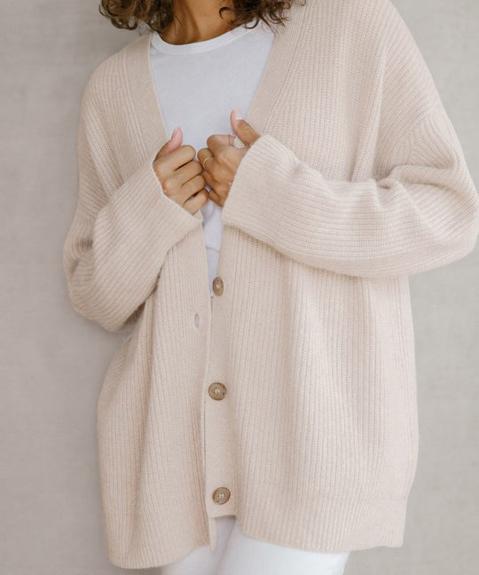 Person wearing a beige cardigan over a white shirt against a neutral background