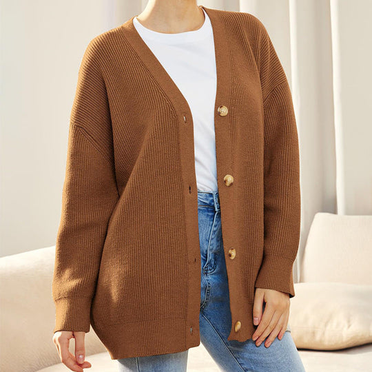Person wearing a brown cardigan over a white shirt and blue jeans in a neutral setting
