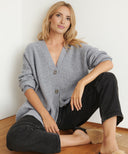 Woman wearing a gray cardigan and black pants sitting on a wooden floor.