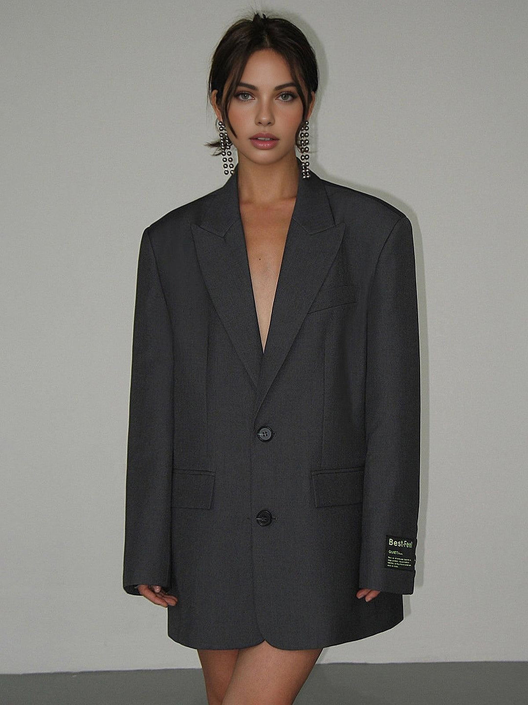 Woman wearing a dark gray blazer with a brand label on a plain background