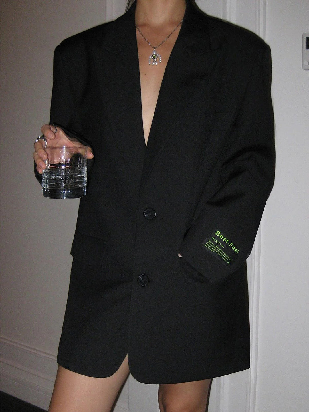 Person wearing a black blazer with a visible brand logo, holding a glass.