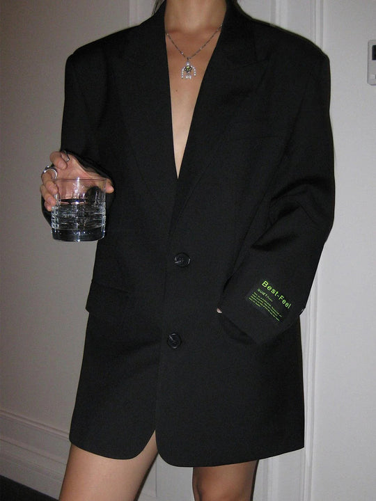 Person wearing a black blazer with a visible brand logo, holding a glass.