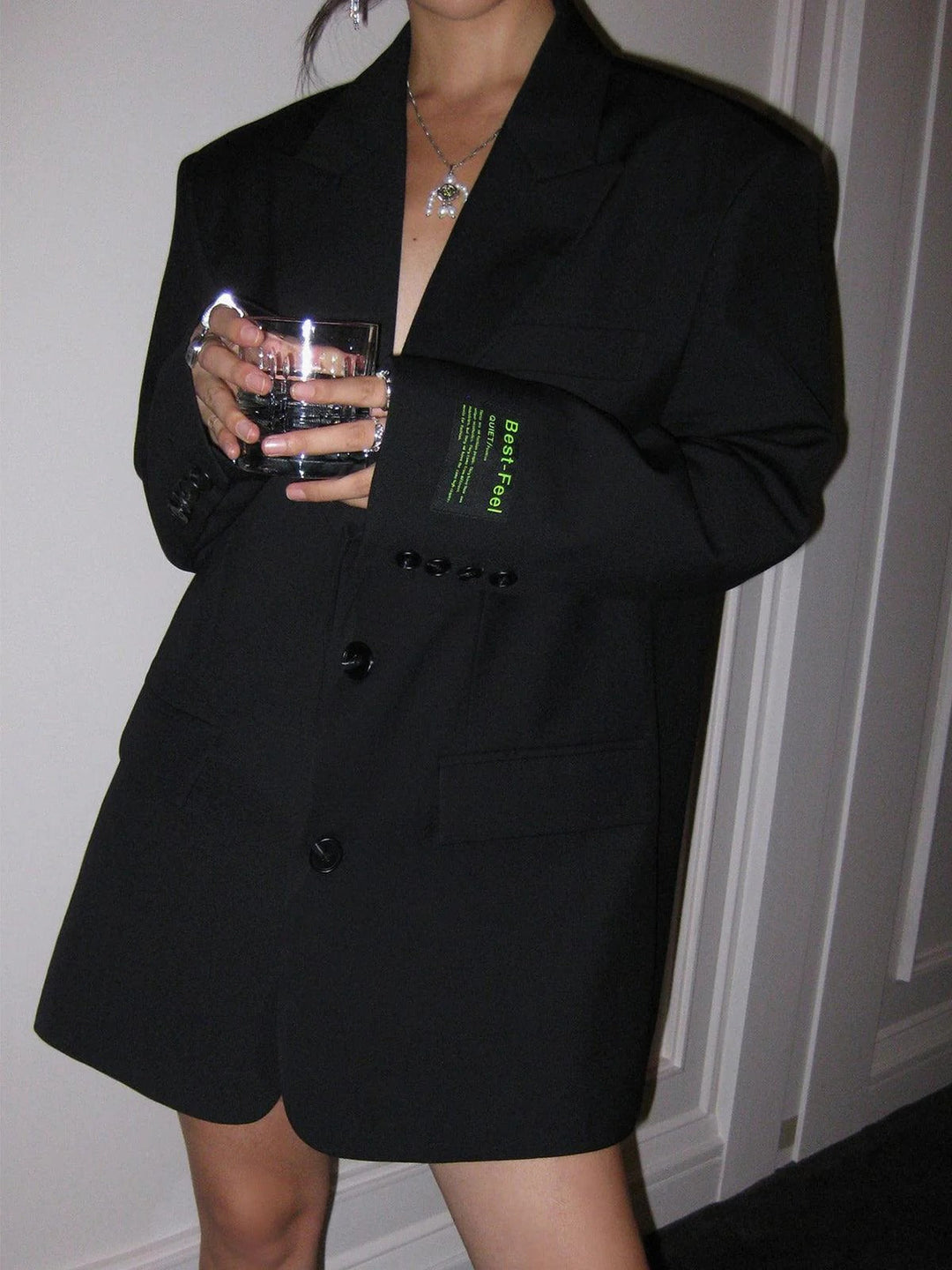 Person wearing a black blazer with text on the sleeve, holding a glass.