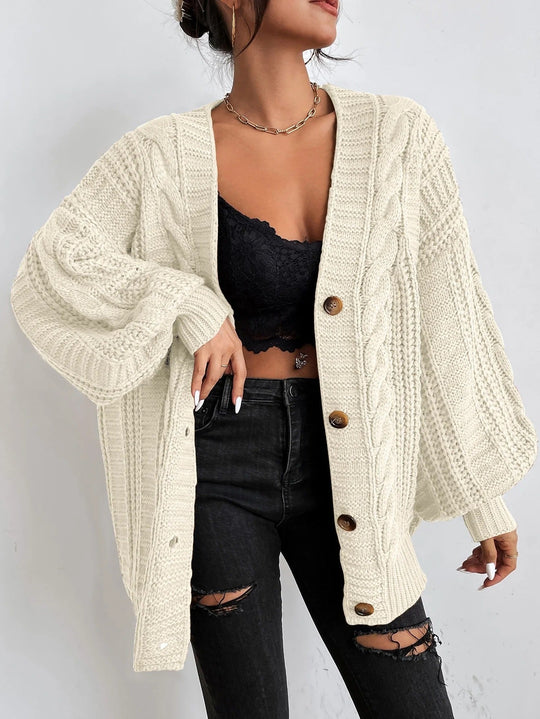Person wearing a cream cable knit cardigan over a black top and jeans on a plain background
