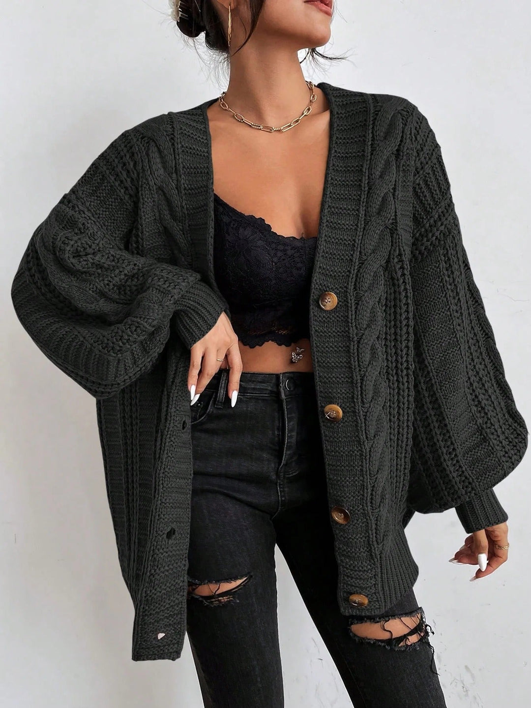 Person wearing a dark green cardigan over a black top and jeans on a white background