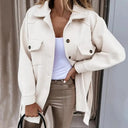 Person wearing a white coat over a light blue top and beige pants, standing indoors.