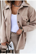 Person wearing a beige coat over a white top and beige pants on a plain background
